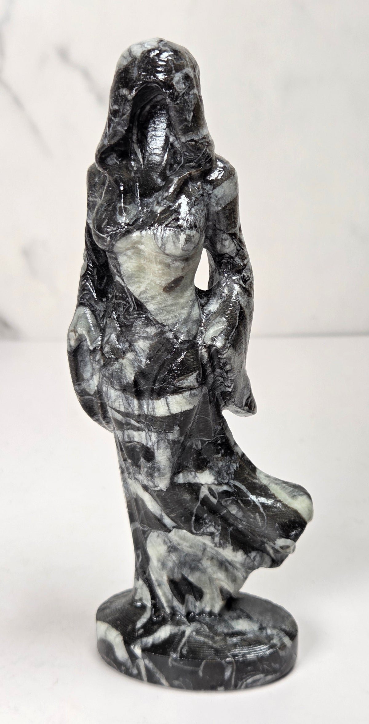 crystal carving of a faceless woman wearing a flowy robe with black and white marbled coloring against a white background
