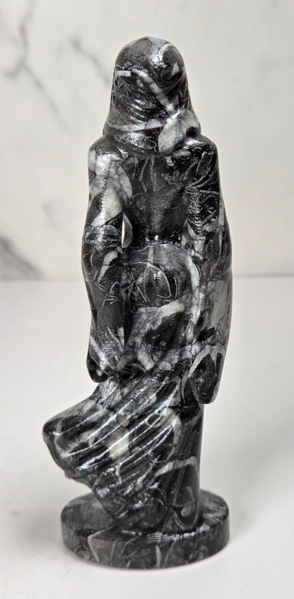 crystal carving of a faceless woman wearing a flowy robe with black and white marbled coloring against a white background