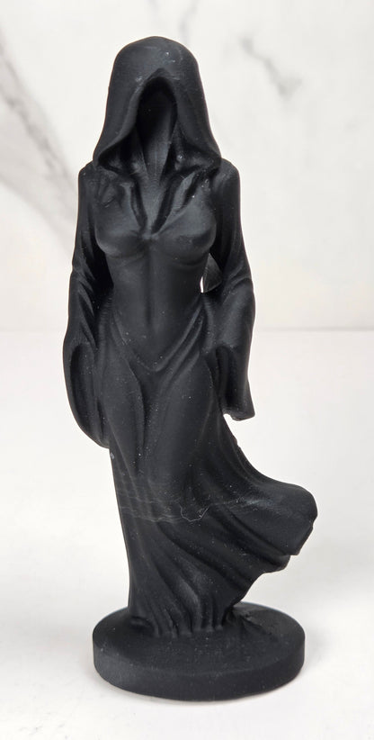 crystal carving of a faceless woman wearing a flowy robe with black coloring against a white background