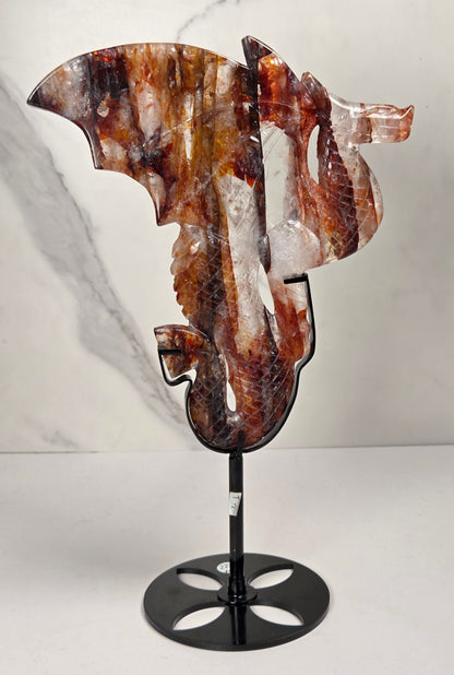 Quartz dragon carving with red and orange inclusions in a black stand against a marbled background