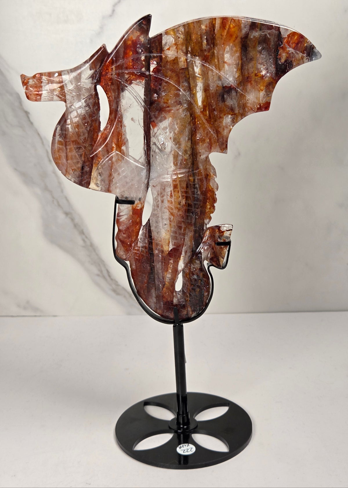 Quartz dragon carving with red and orange inclusions in a black stand against a marbled background