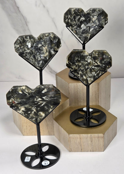 Green and white crystal heart carvings in black stands on a wooden hexagonal stand against a marbled background