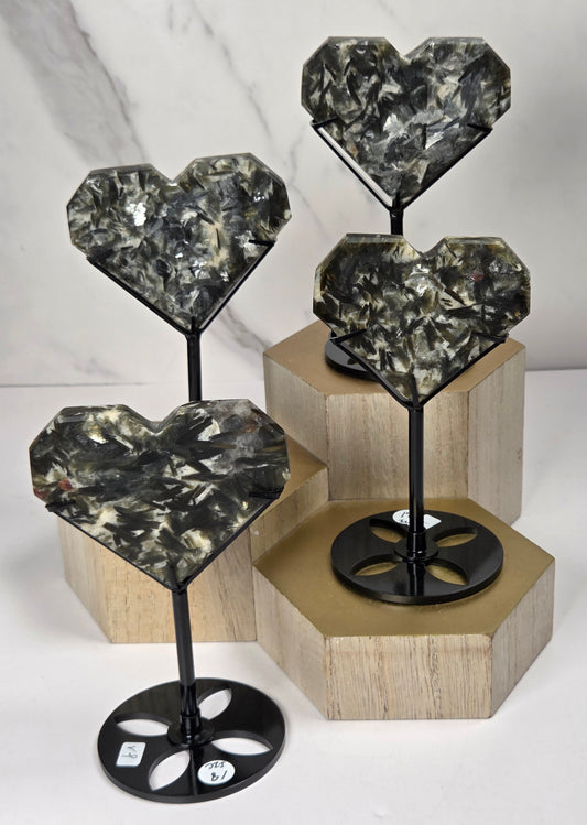 Green and white crystal heart carvings in black stands on a wooden hexagonal stand against a marbled background