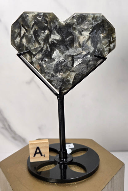 Green and white crystal heart carving in a black stand on a wooden hexagonal stand against a marbled background