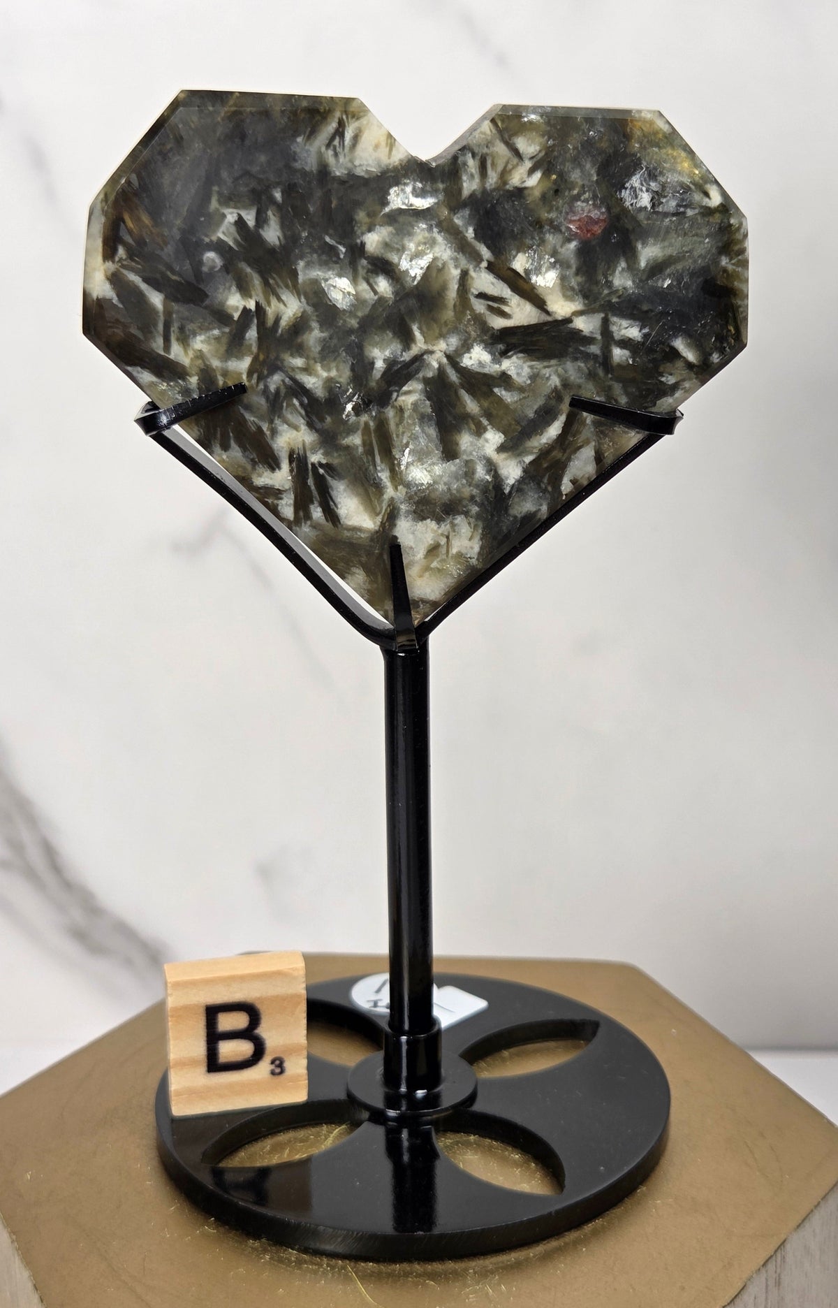 Green and white crystal heart carving in a black stand on a wooden hexagonal stand against a marbled background