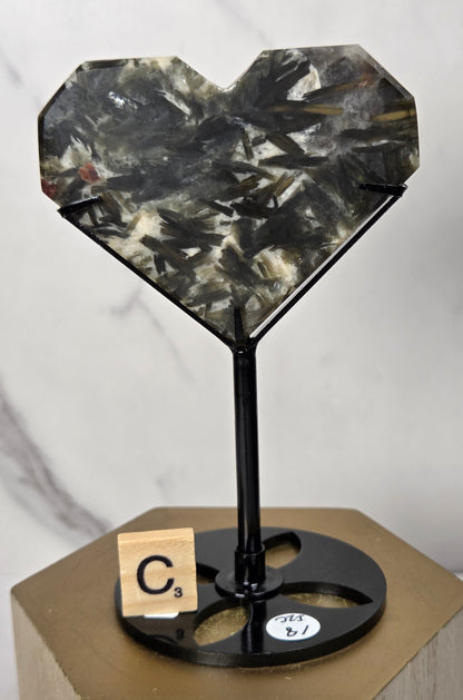 Green and white crystal heart carving in a black stand on a wooden hexagonal stand against a marbled background