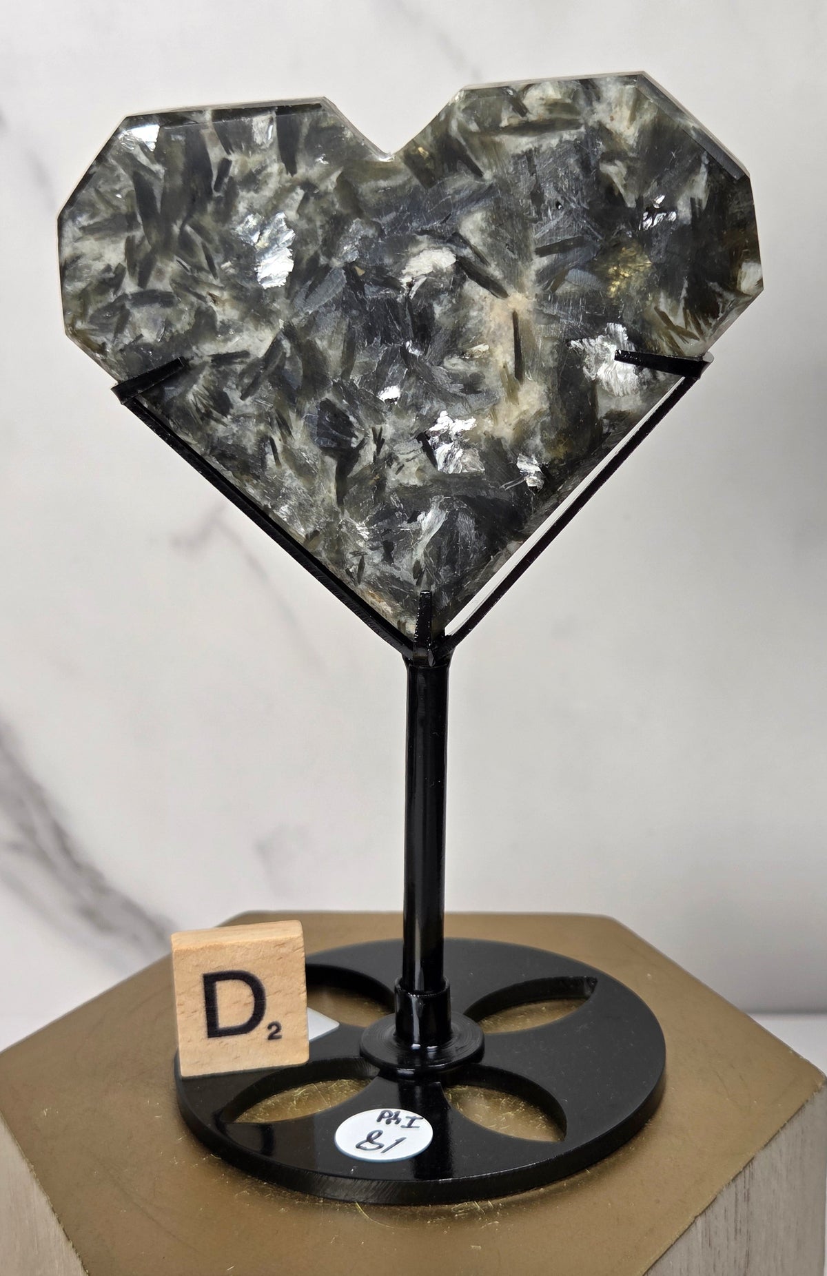 Green and white crystal heart carving in a black stand on a wooden hexagonal stand against a marbled background