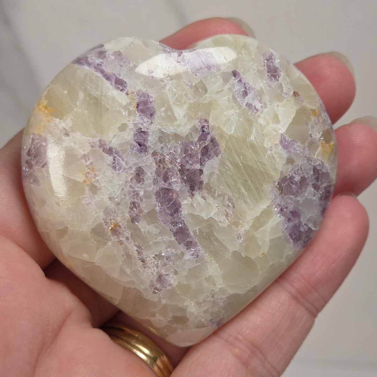 Hand holding a white crystal heart with purple coloring against a marbled background