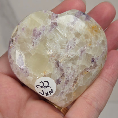 Hand holding a white crystal heart with purple coloring against a marbled background