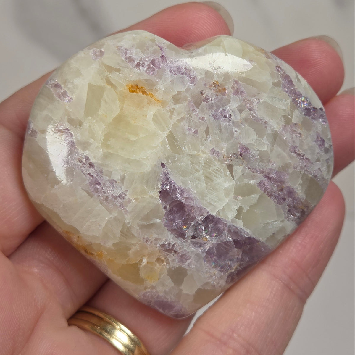 Hand holding a white crystal heart with purple coloring against a marbled background