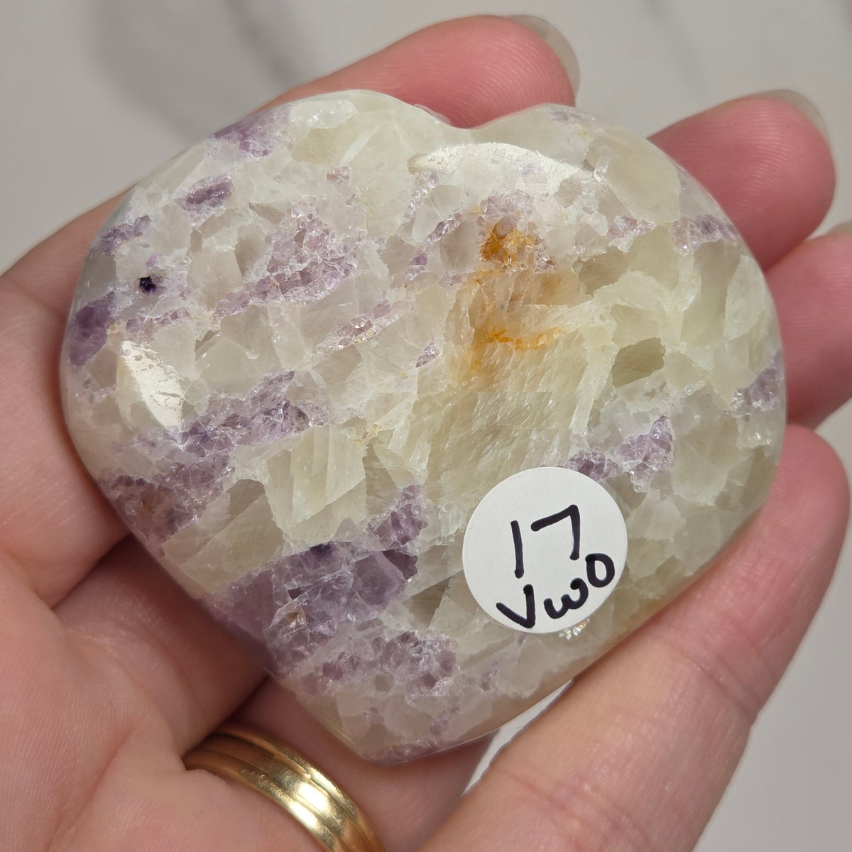 Hand holding a white crystal heart with purple coloring against a marbled background