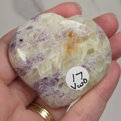 Hand holding a white crystal heart with purple coloring against a marbled background