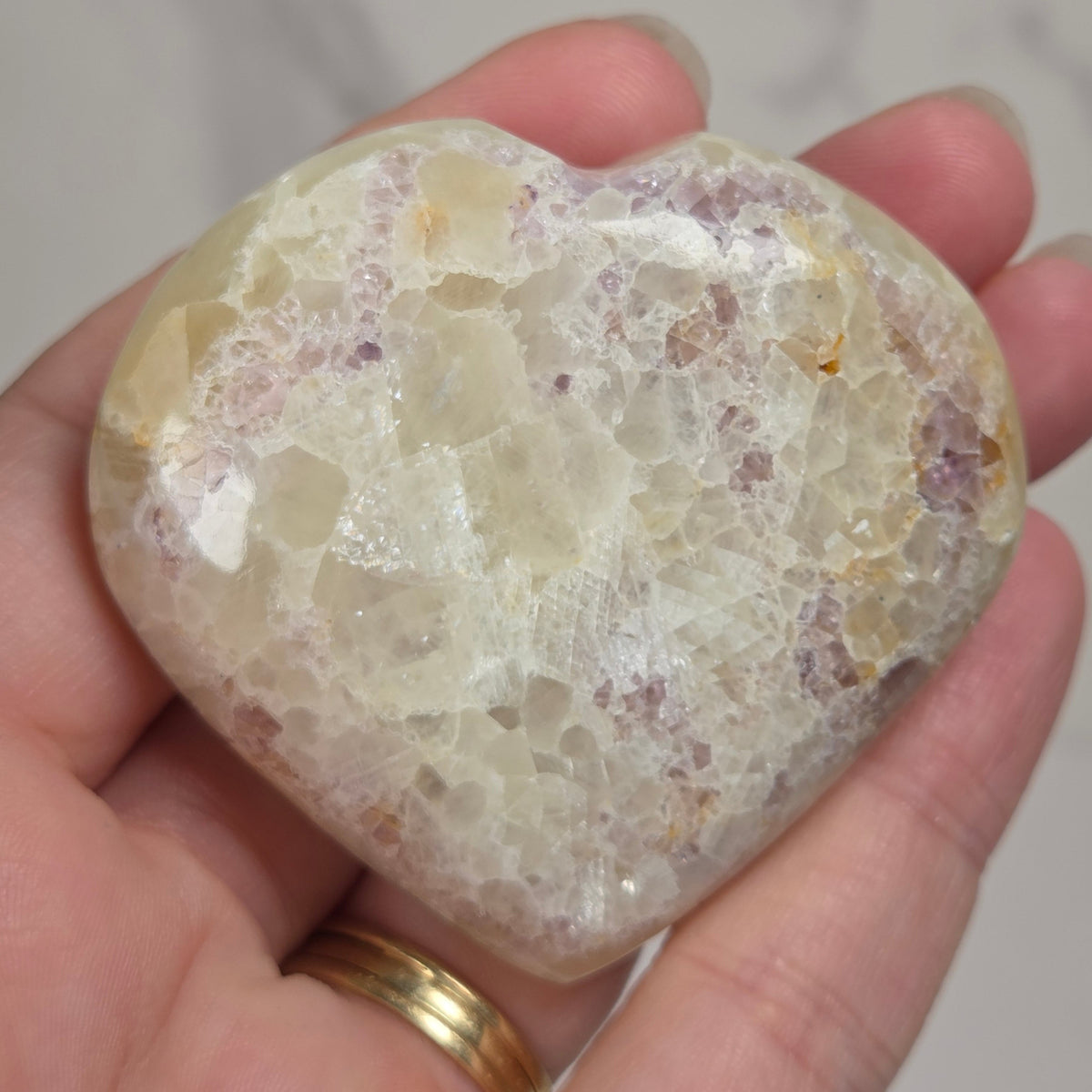 Hand holding a white crystal heart with purple coloring against a marbled background