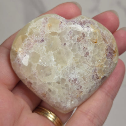 Hand holding a white crystal heart with purple coloring against a marbled background