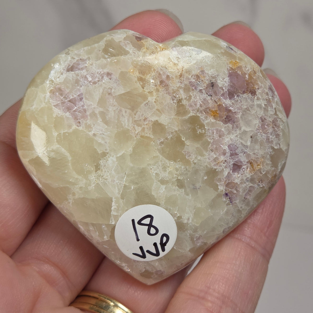 Hand holding a white crystal heart with purple coloring against a marbled background