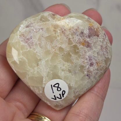 Hand holding a white crystal heart with purple coloring against a marbled background