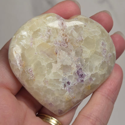 Hand holding a white crystal heart with purple coloring against a marbled background