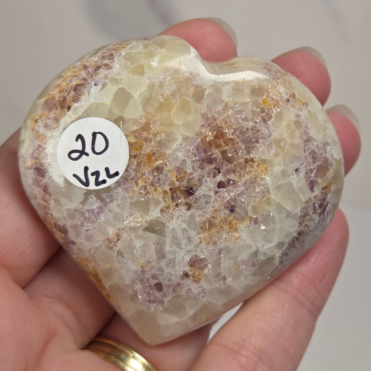 Hand holding a white crystal heart with purple coloring against a marbled background