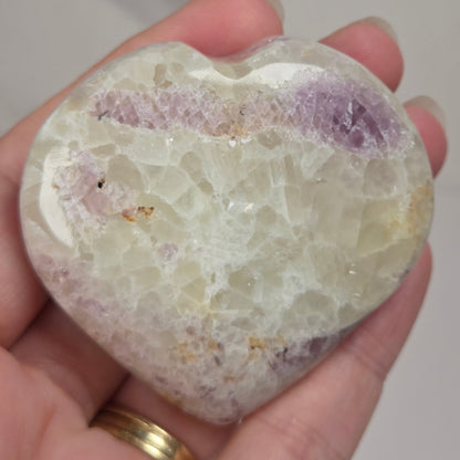 Hand holding a white crystal heart with purple coloring against a marbled background