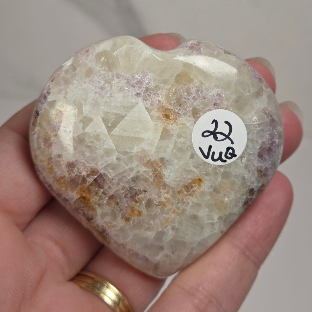 Hand holding a white crystal heart with purple coloring against a marbled background