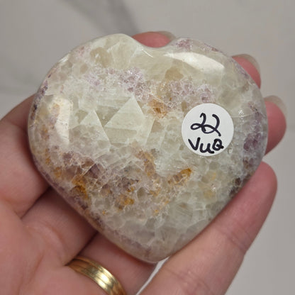 Hand holding a white crystal heart with purple coloring against a marbled background