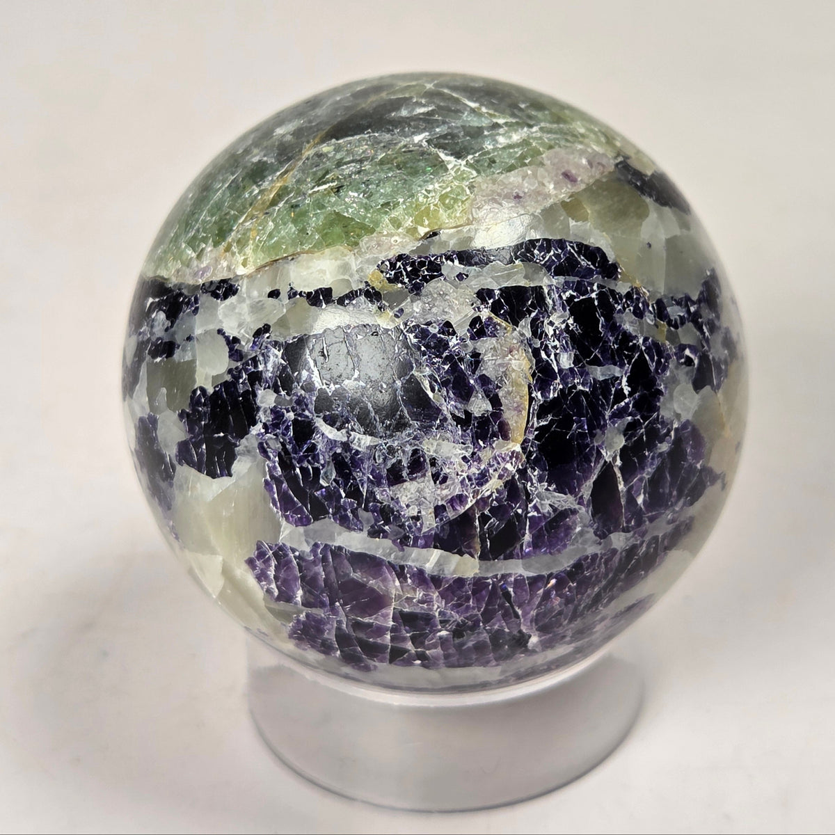 Crystal sphere carving with white and green coloring on an acrylic stand against a white background
