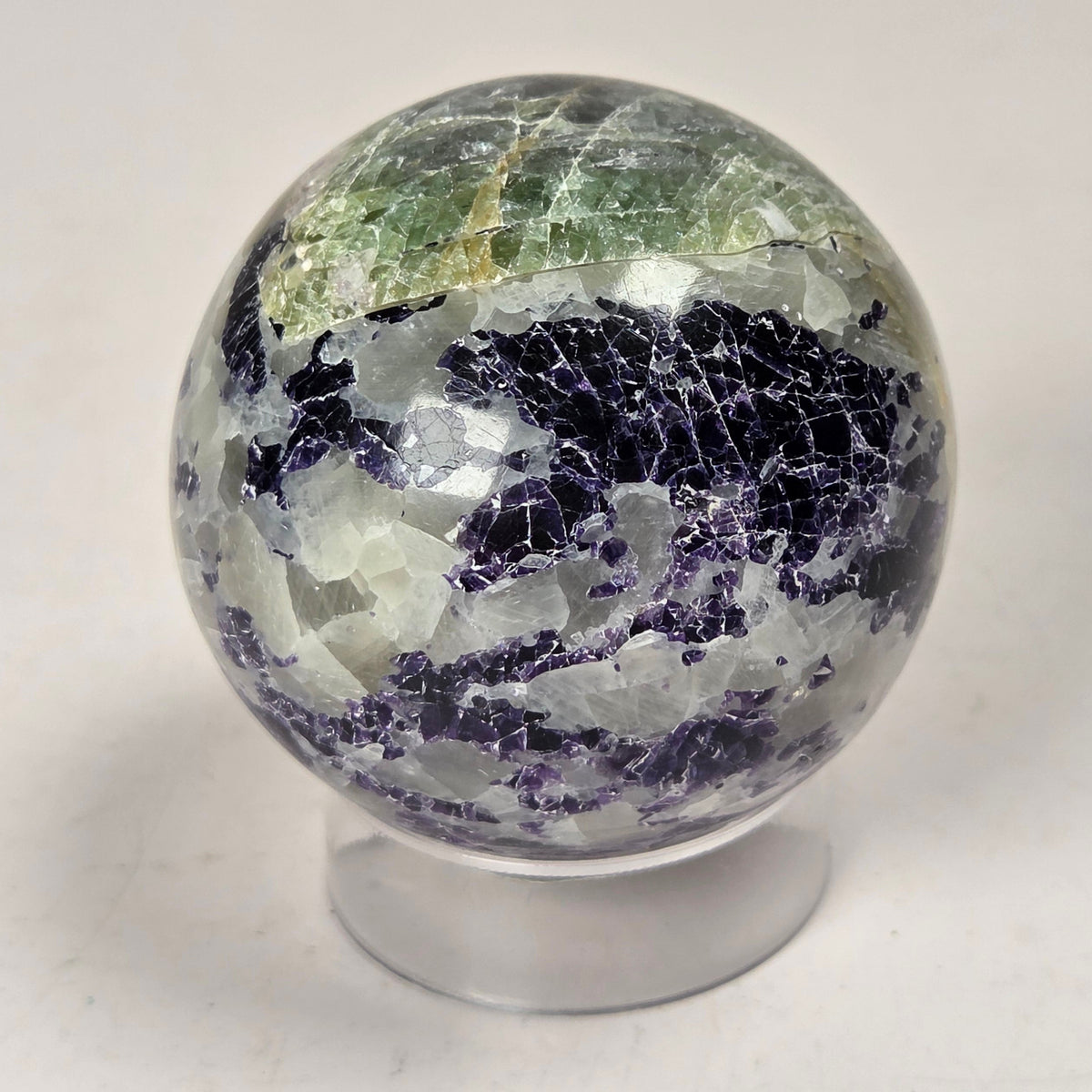 Crystal sphere carving with white and green coloring on an acrylic stand against a white background