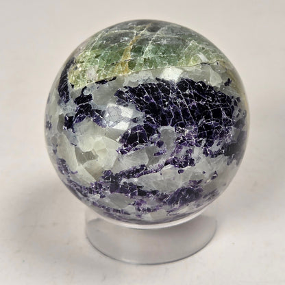 Crystal sphere carving with white and green coloring on an acrylic stand against a white background