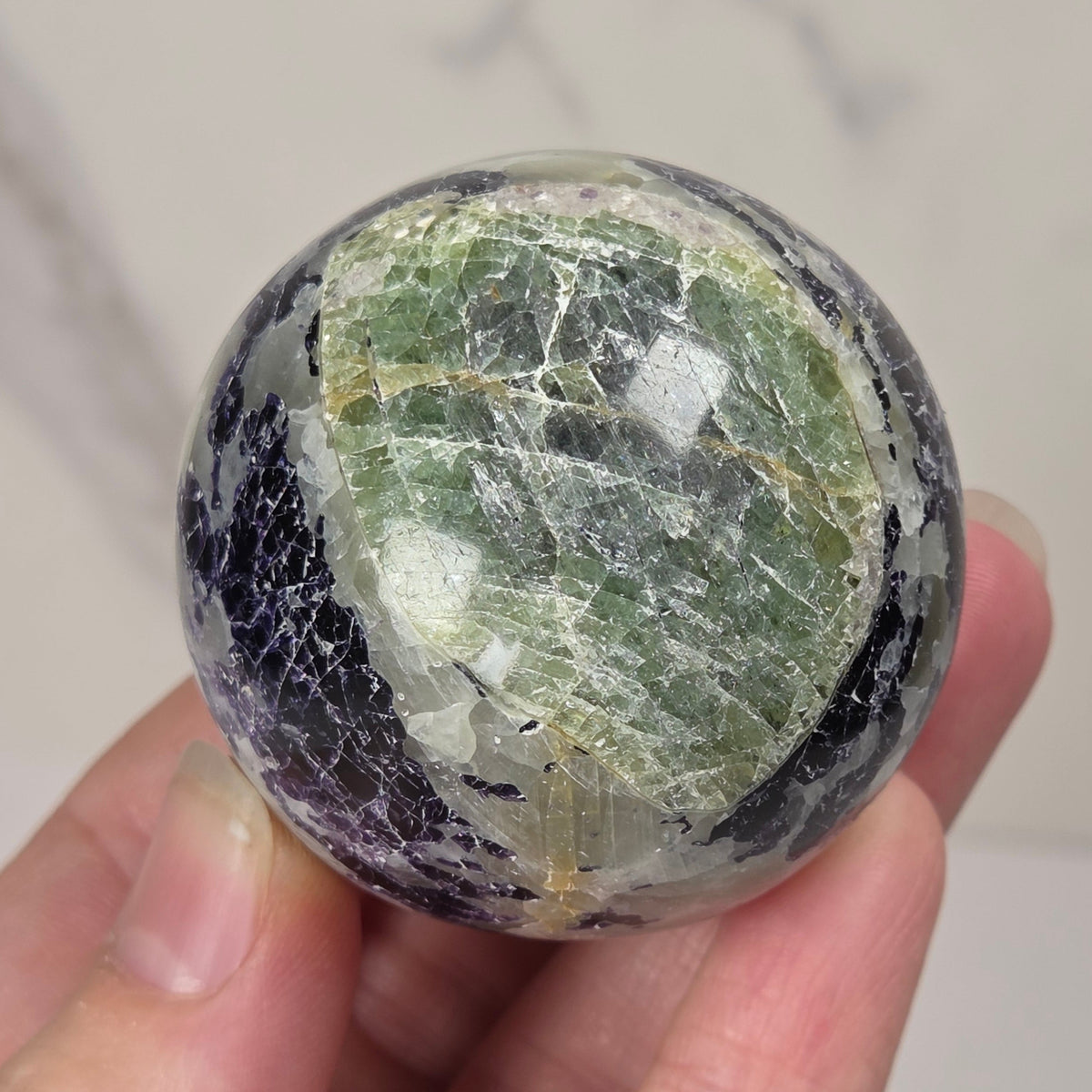 Crystal sphere carving with white and green coloring being held by a hand against a white background