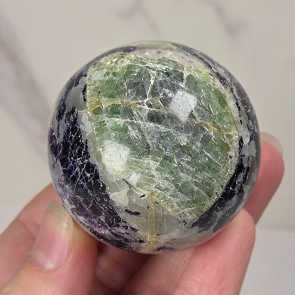 Crystal sphere carving with white and green coloring being held by a hand against a white background