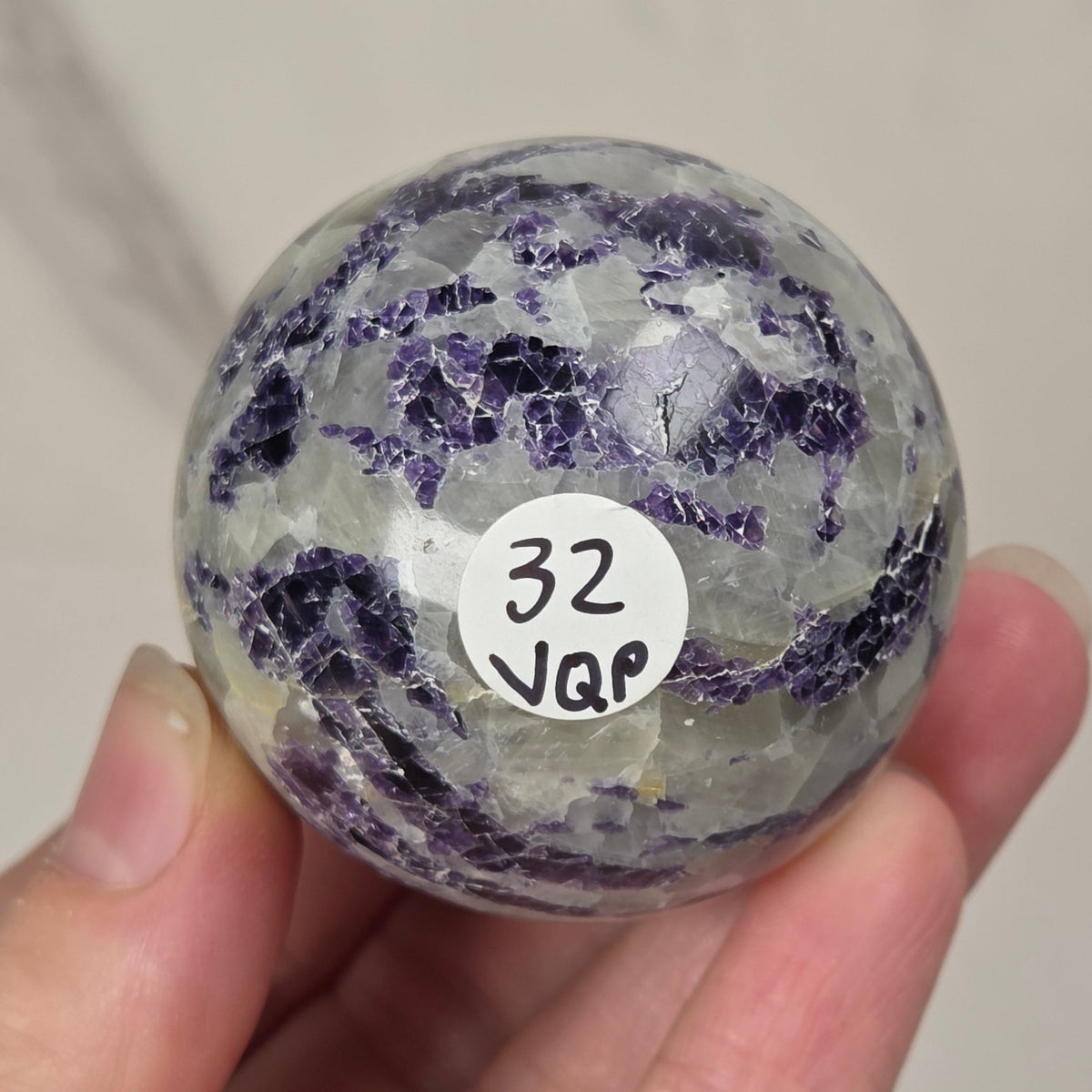 Crystal sphere carving with white and green coloring being held by a hand against a white background