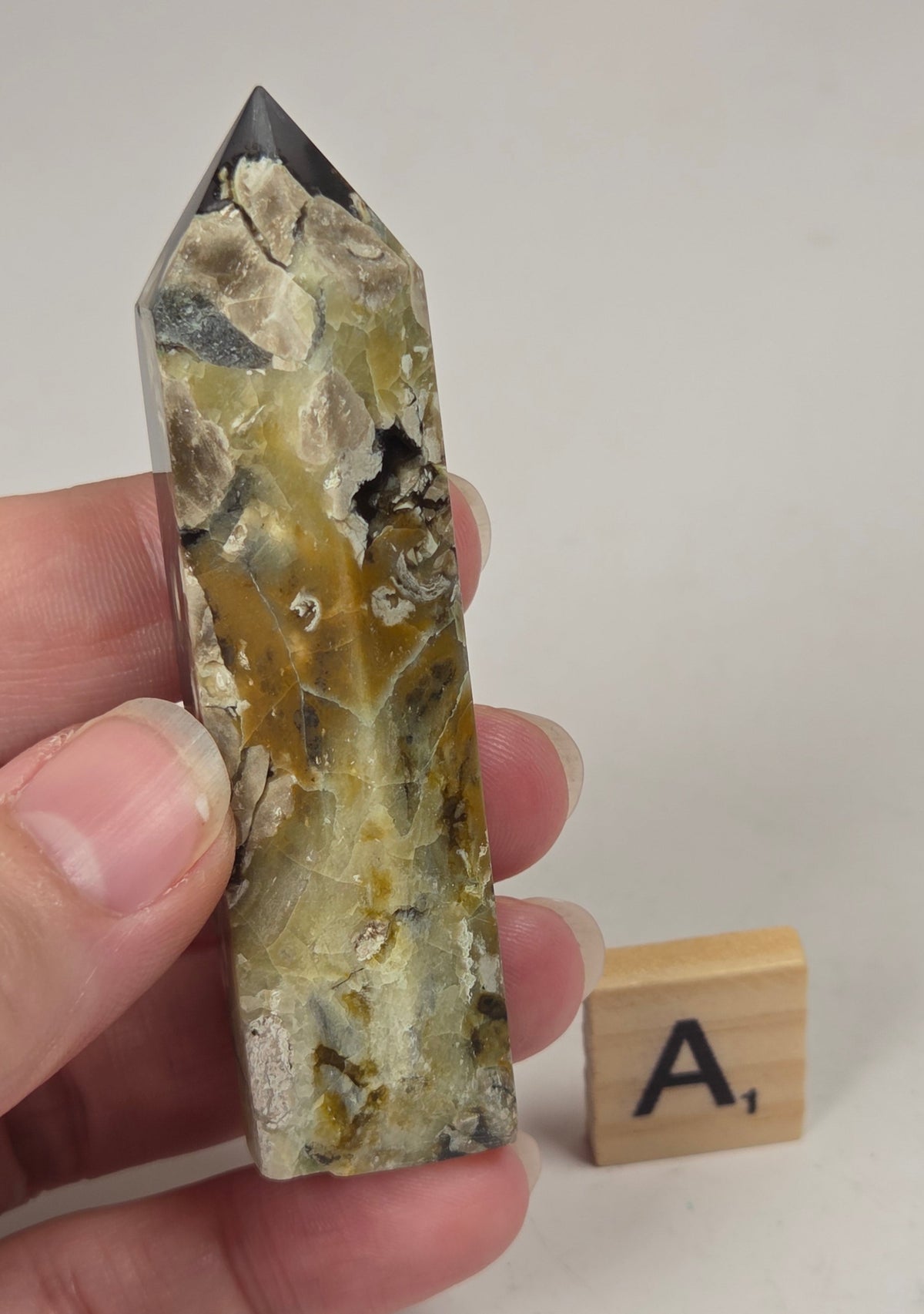 Volcano Agate polished point with tan and black coloring with a scrabble letter against a marbled background