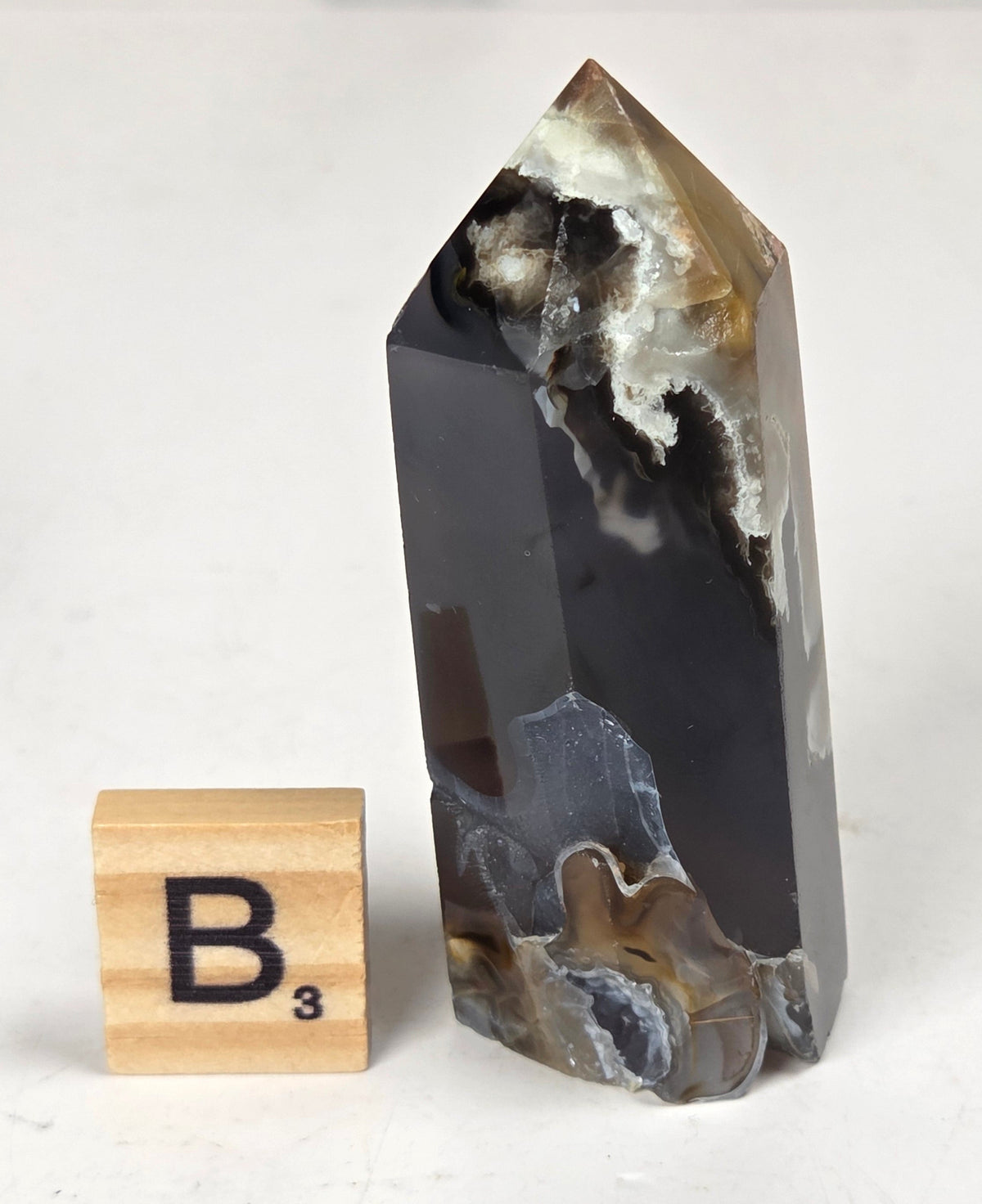 Volcano Agate polished point with tan and black coloring with a scrabble letter against a marbled background