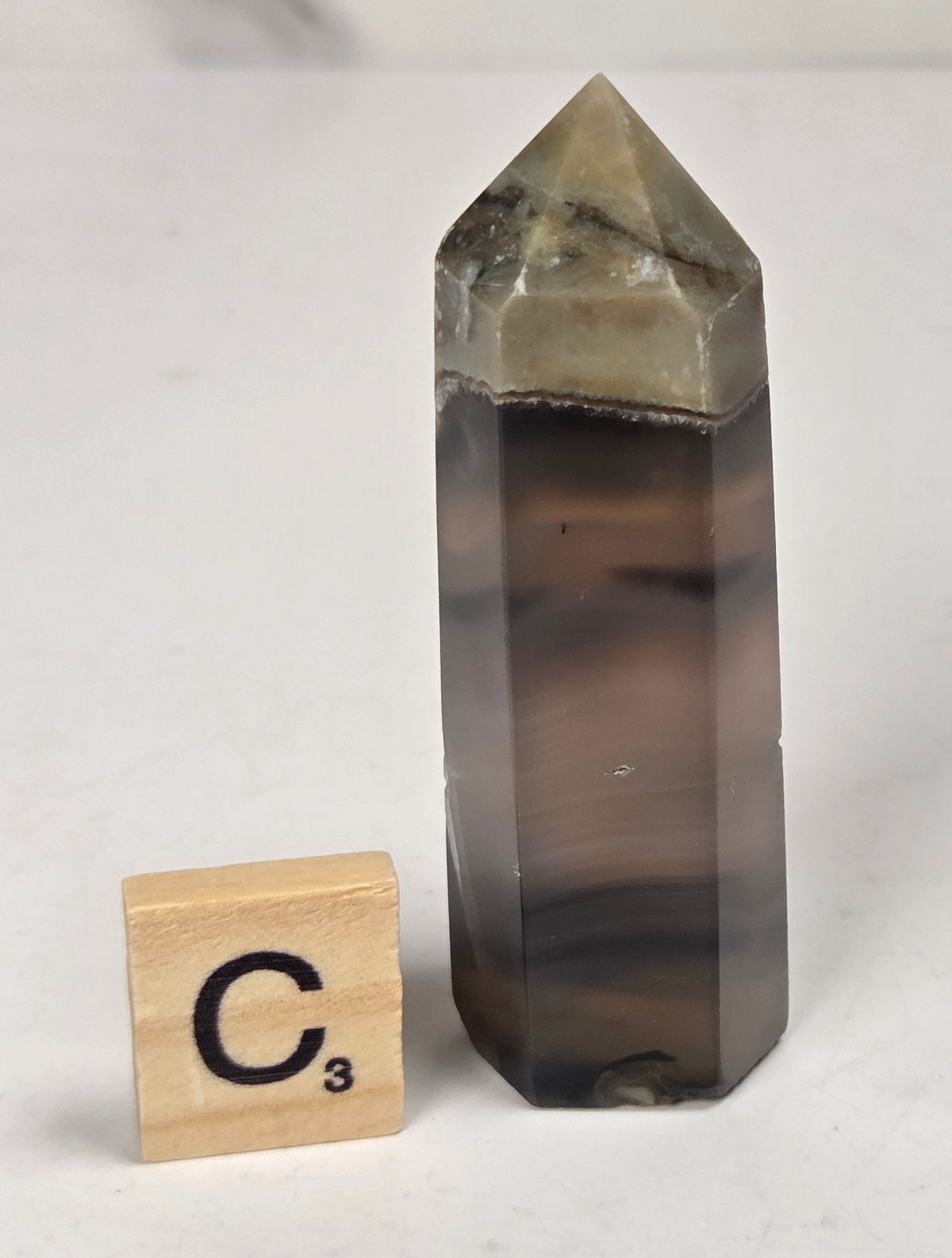 Volcano Agate polished point with tan and black coloring with a scrabble letter against a marbled background