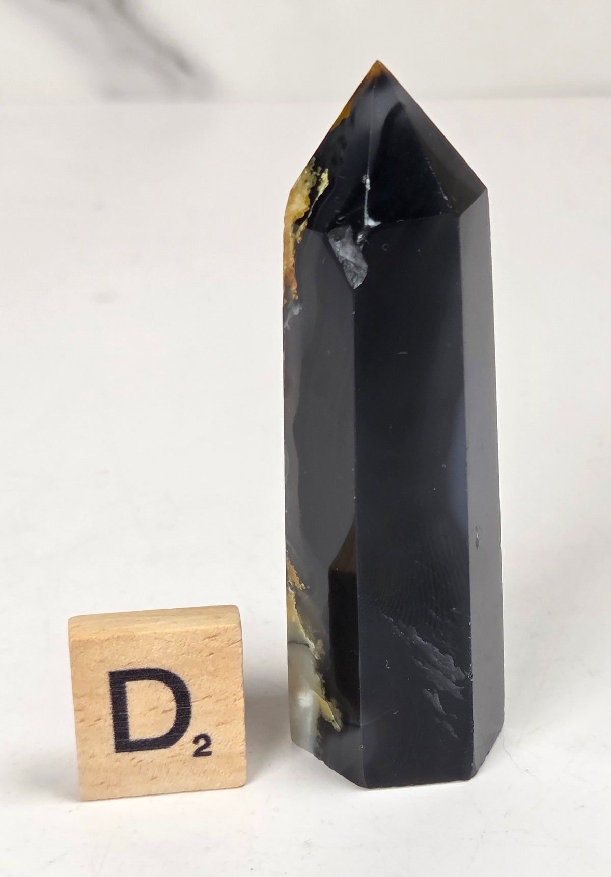 Volcano Agate polished point with tan and black coloring with a scrabble letter against a marbled background