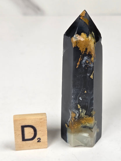 Volcano Agate polished point with tan and black coloring with a scrabble letter against a marbled background