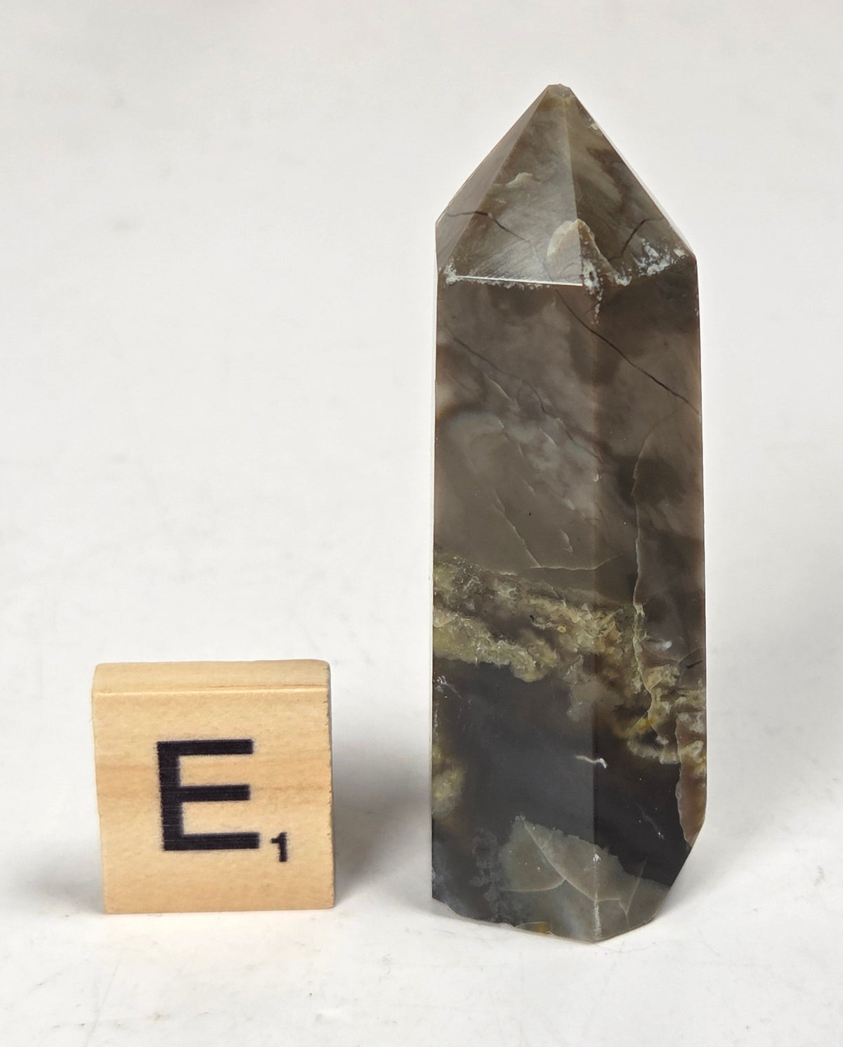 Volcano Agate polished point with tan and black coloring with a scrabble letter against a marbled background