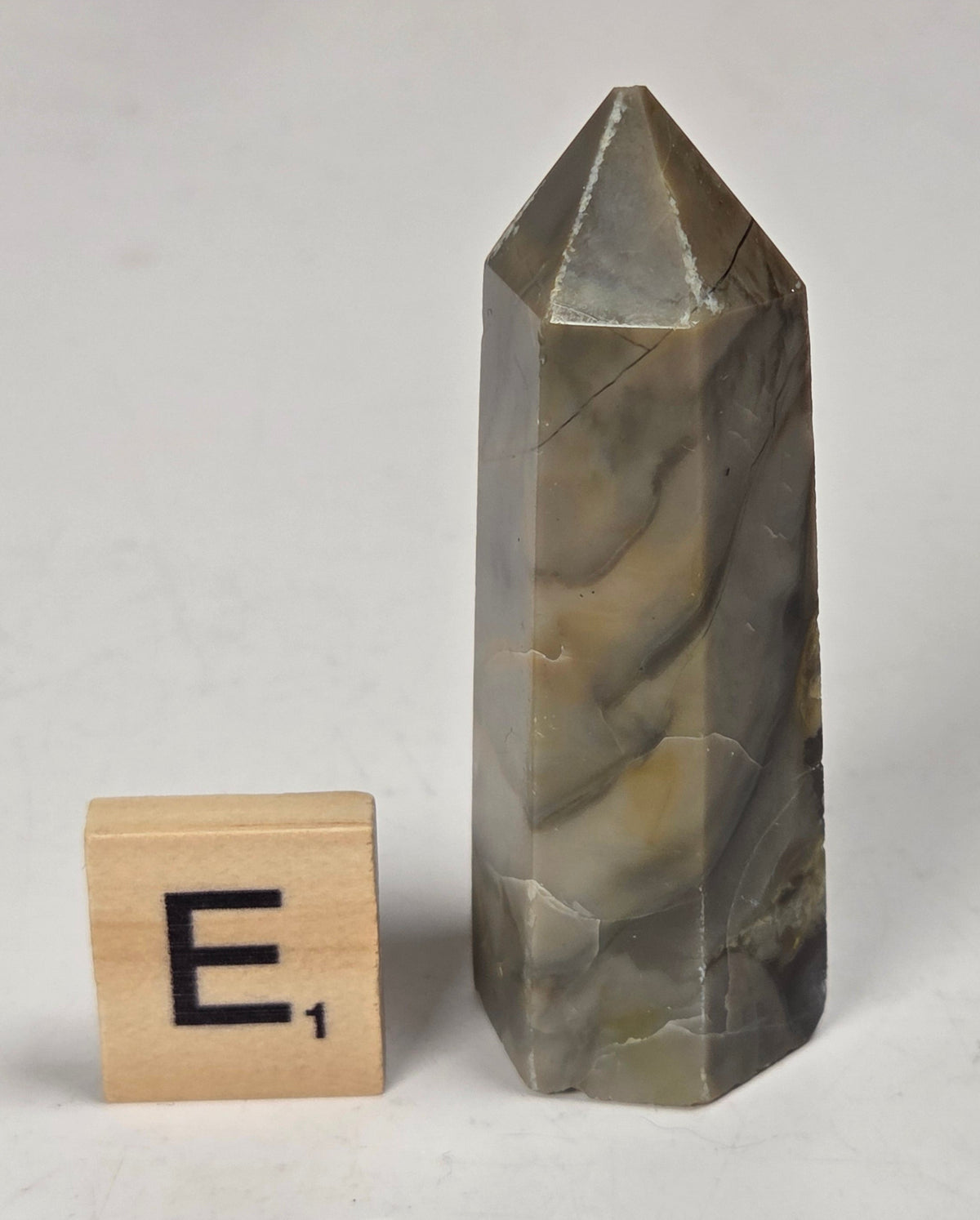 Volcano Agate polished point with tan and black coloring with a scrabble letter against a marbled background