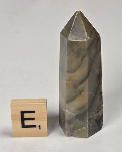Volcano Agate polished point with tan and black coloring with a scrabble letter against a marbled background