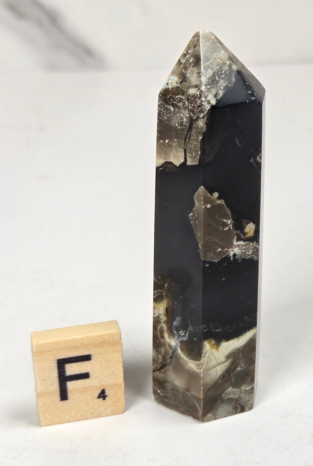 Volcano Agate polished point with tan and black coloring with a scrabble letter against a marbled background