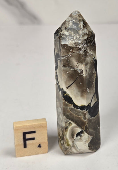 Volcano Agate polished point with tan and black coloring with a scrabble letter against a marbled background