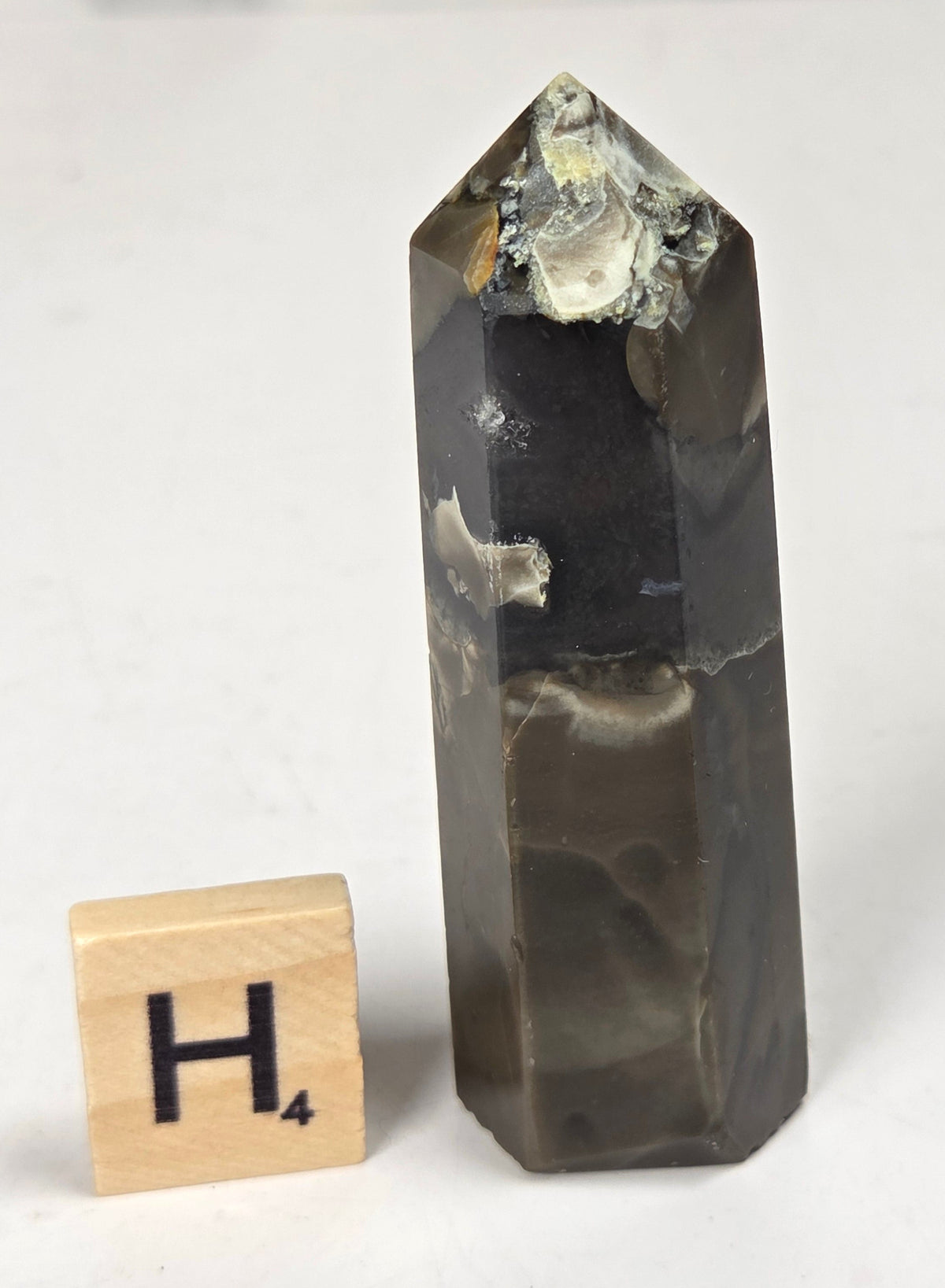 Volcano Agate polished point with tan and black coloring with a scrabble letter against a marbled background