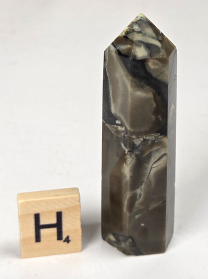 Volcano Agate polished point with tan and black coloring with a scrabble letter against a marbled background