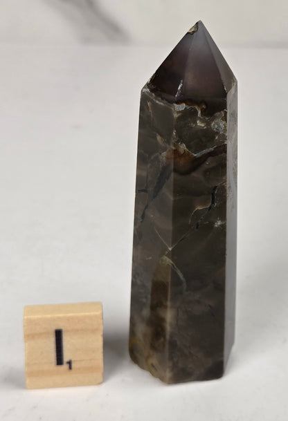 Volcano Agate polished point with tan and black coloring with a scrabble letter against a marbled background