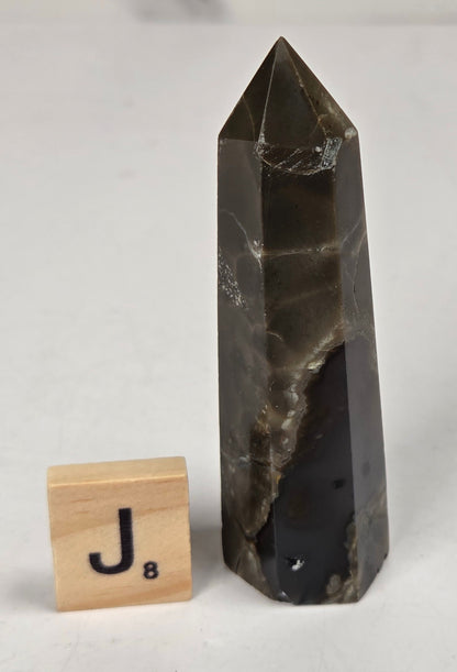 Volcano Agate polished point with tan and black coloring with a scrabble letter against a marbled background