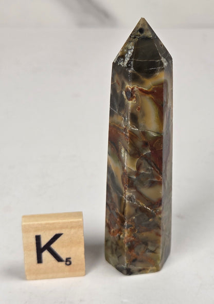 Volcano Agate polished point with tan and black coloring with a scrabble letter against a marbled background
