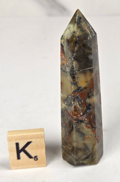 Volcano Agate polished point with tan and black coloring with a scrabble letter against a marbled background