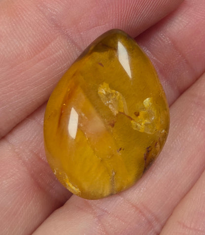 Clear quartz teardrrop shaped crystal with gold rutile inclusions held between fingers