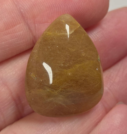 Clear quartz teardrrop shaped crystal with gold rutile inclusions held between fingers
