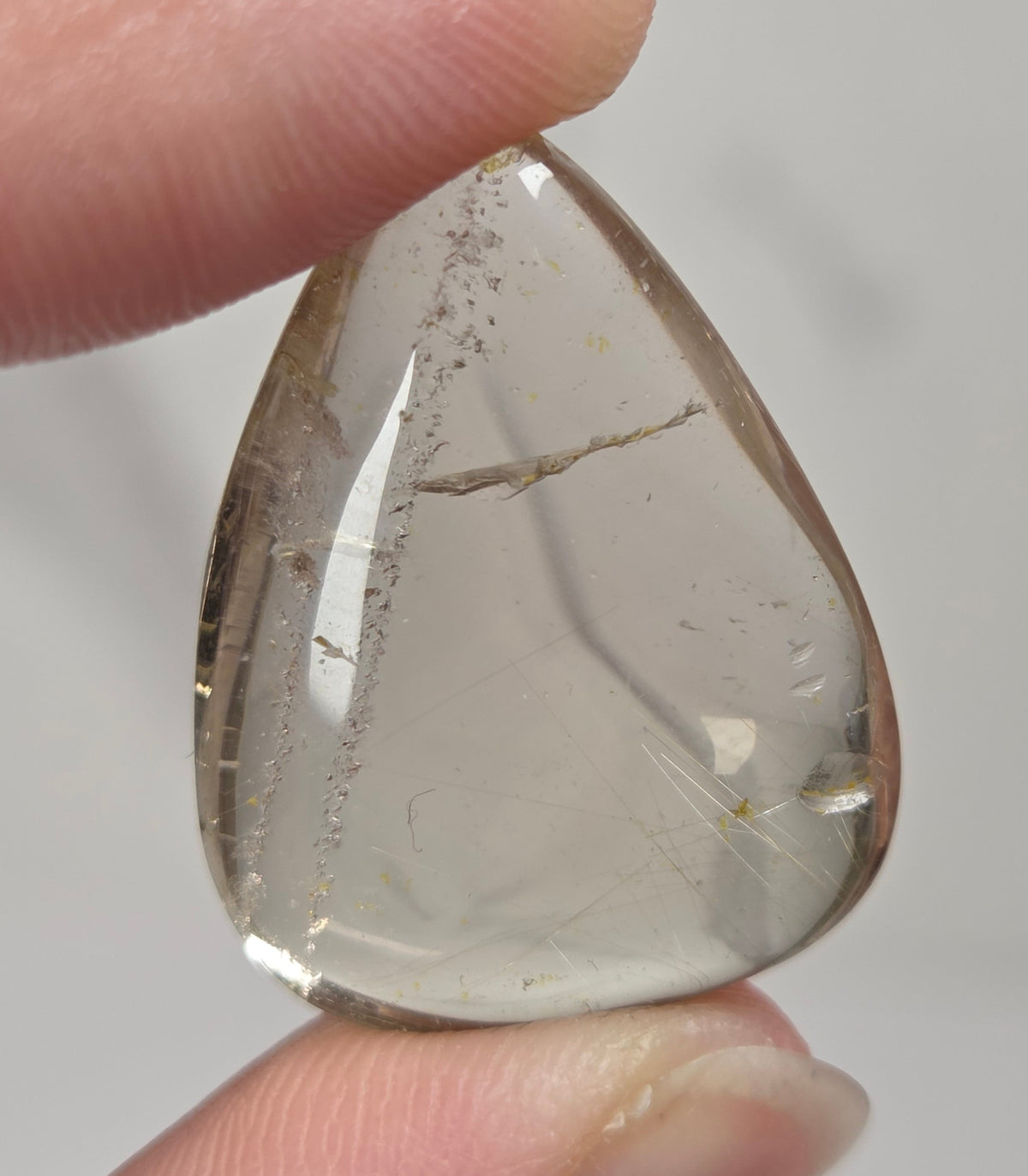 Clear quartz teardrrop shaped crystal with gold rutile inclusions held between fingers
